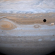 Jupiter's moon Io passes in front of the gas giant, casting its shadow on the planet's surface.